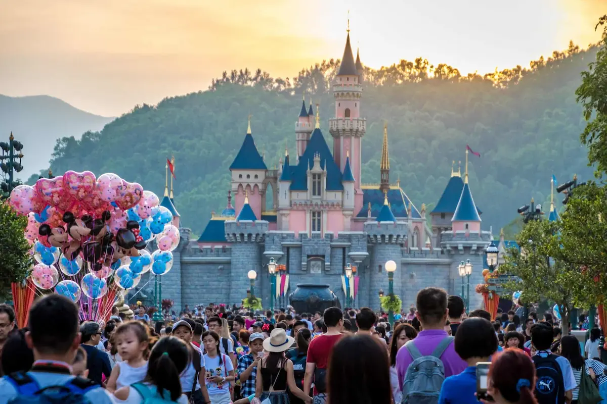 Crowd walking toward the castle at Hong Kong Disneyland during sunset.