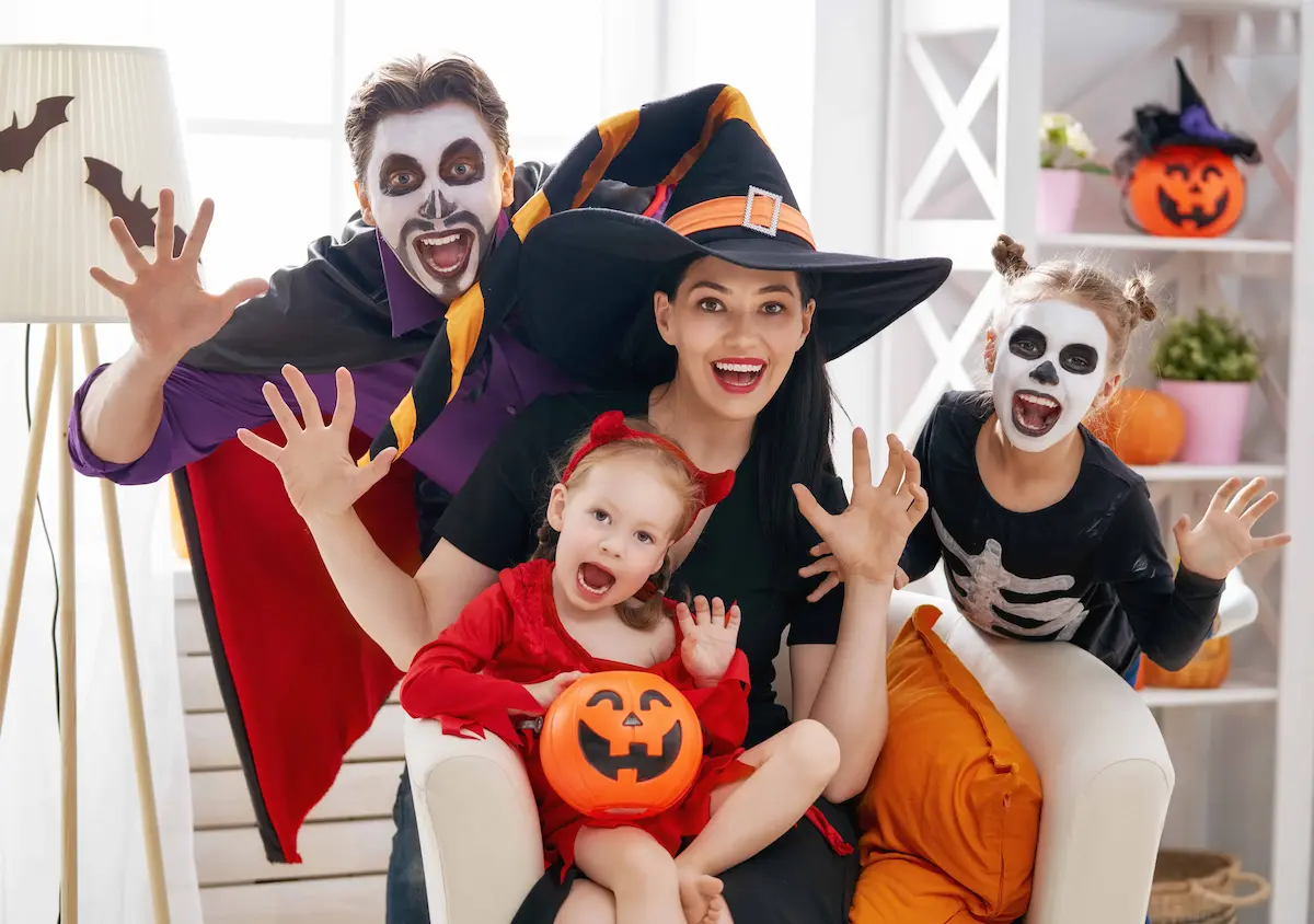 Happy family in Halloween costumes posing indoors with pumpkin bucket