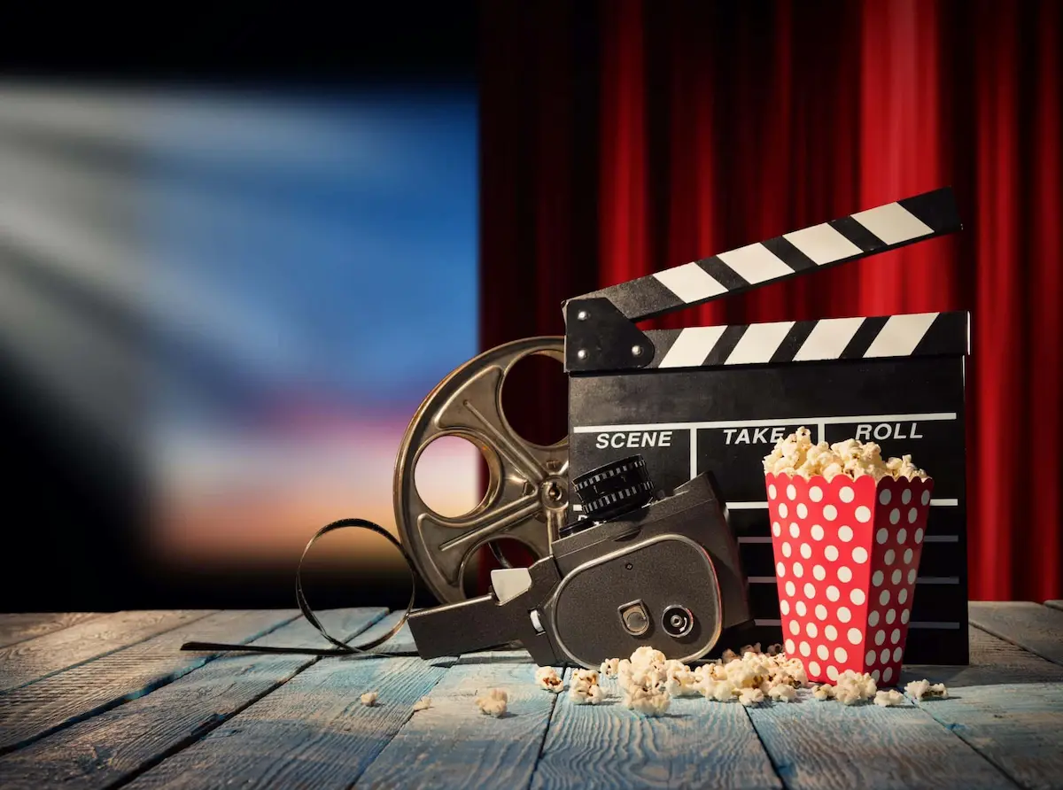 Movie-themed setup with film reel, clapperboard, and popcorn in a cinema setting.