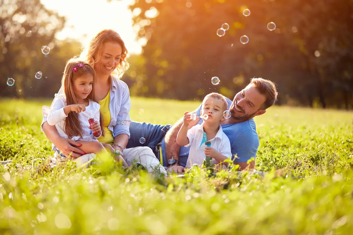 Happy family with children playing bubbles outdoors at sunset