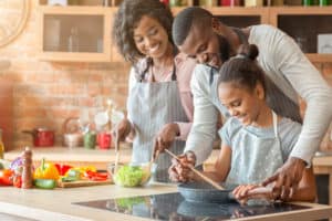 shutterstock 1526428205 Kind,Afro,Parents,Teaching,Their,Adorable,Daughter,How,To,Cook