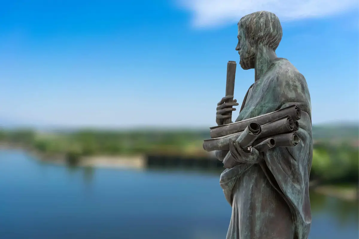 Bronze statue of ancient philosopher holding scrolls near waterfront
