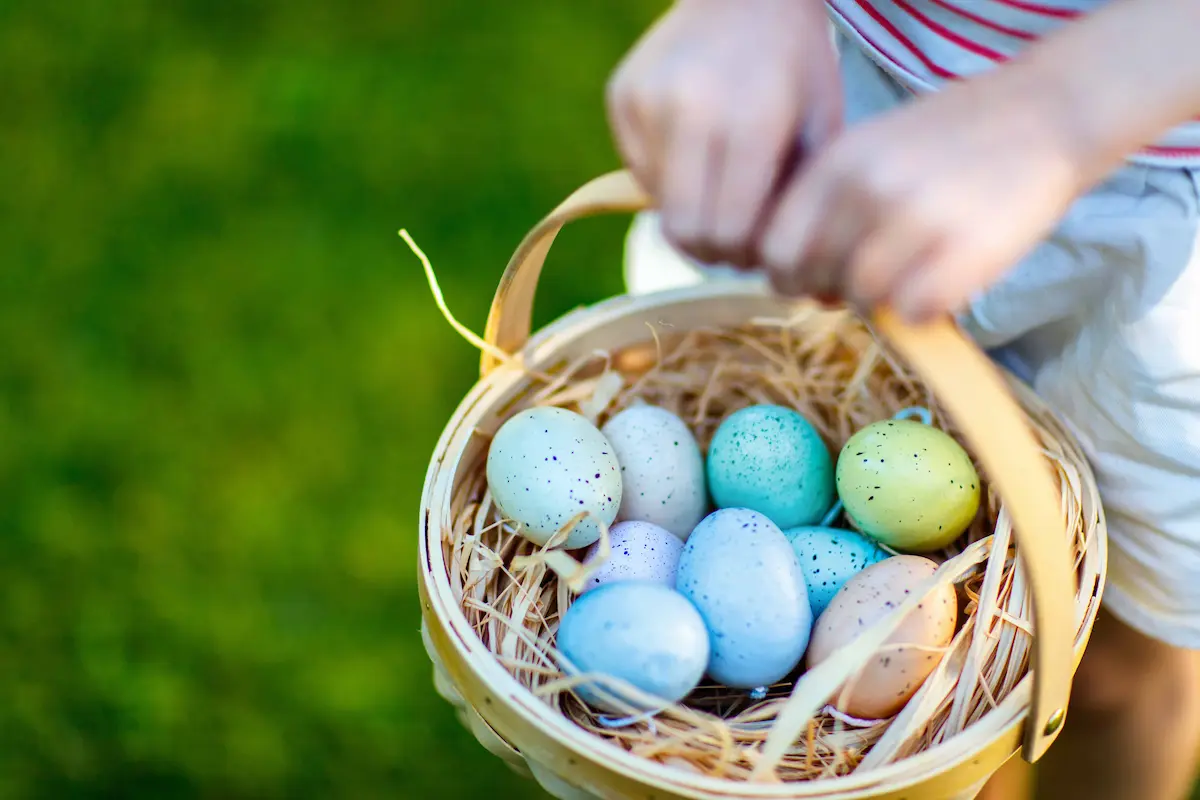 Child carrying a basket filled with colorful Easter eggs during an outdoor Easter egg hunt