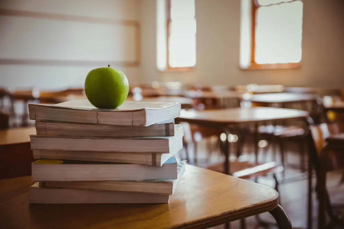 Stack of school books with green apple in classroom setting