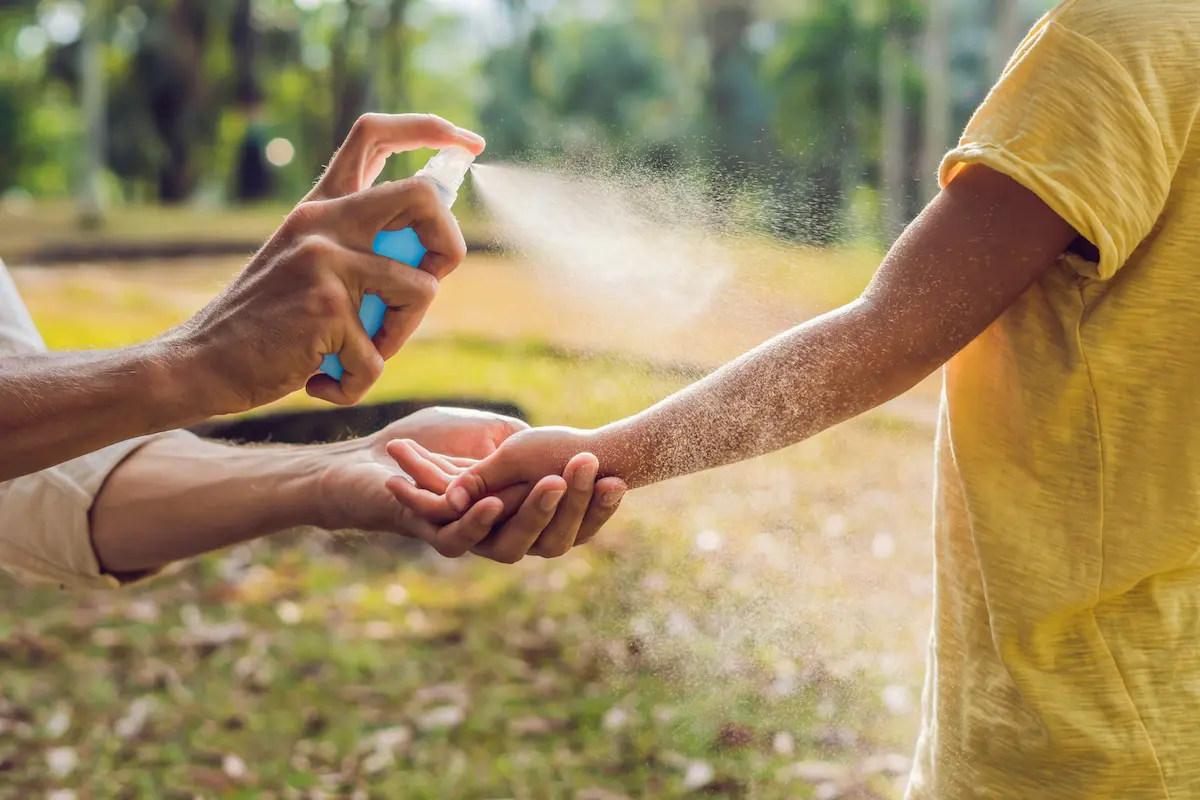 Applying mosquito repellent spray on a child’s arm outdoors