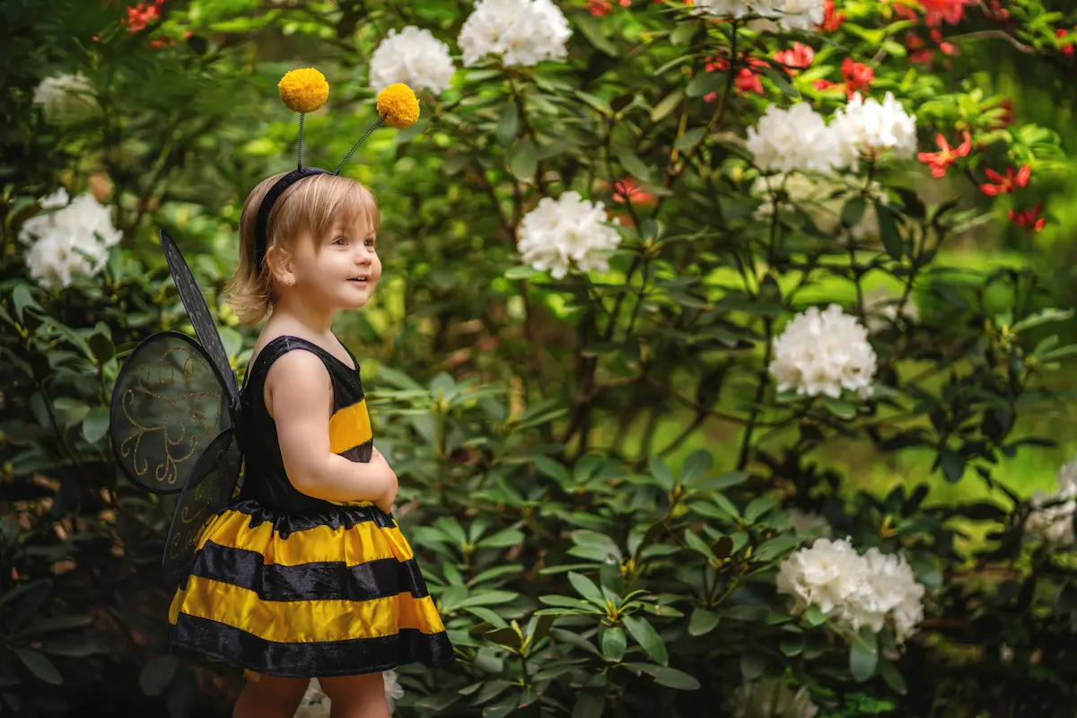 Young child wearing a bee costume standing in a flower garden