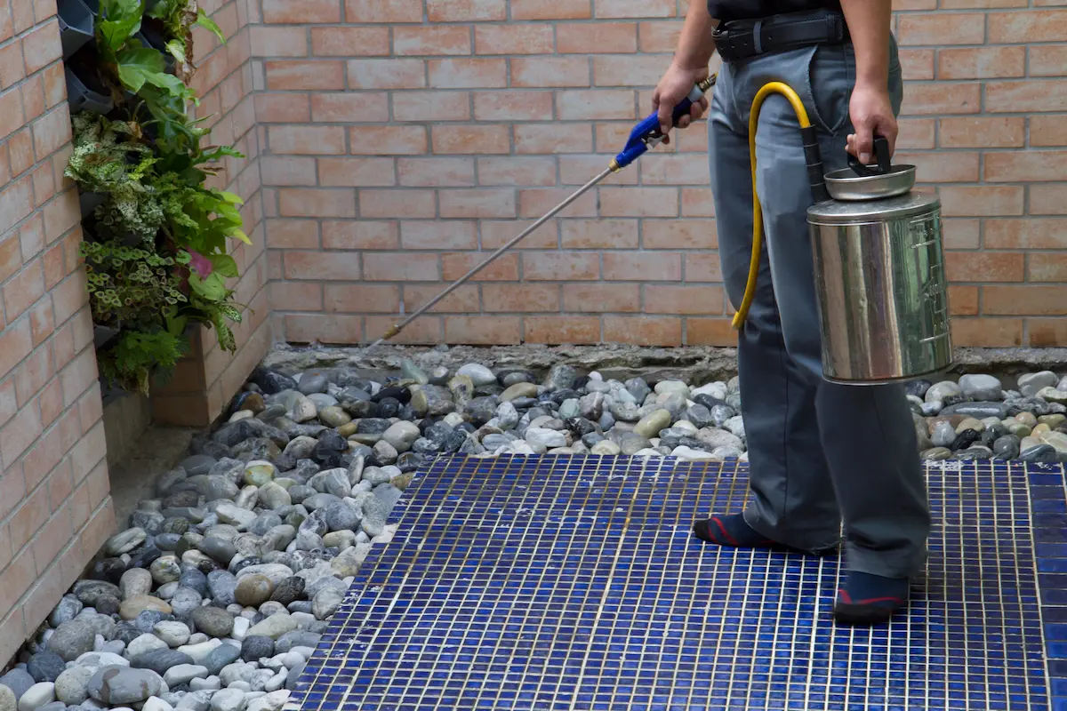 Pest control technician spraying outdoor treatment around residential property